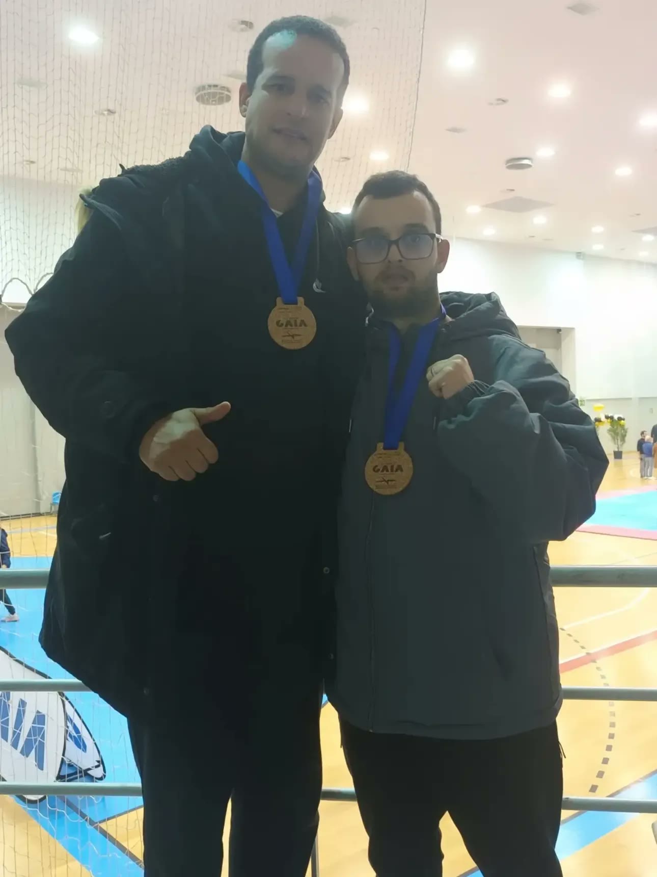Frederico com medalha de ouro ao peito, de punho erguido, ao lado do treinador